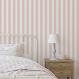 Bedroom with pink and white striped wallpaper, bed with striped bedding, and wooden nightstand.
