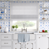White farmhouse kitchen with Delft tile wallpaper in blue and white floral design behind sink and shelves.