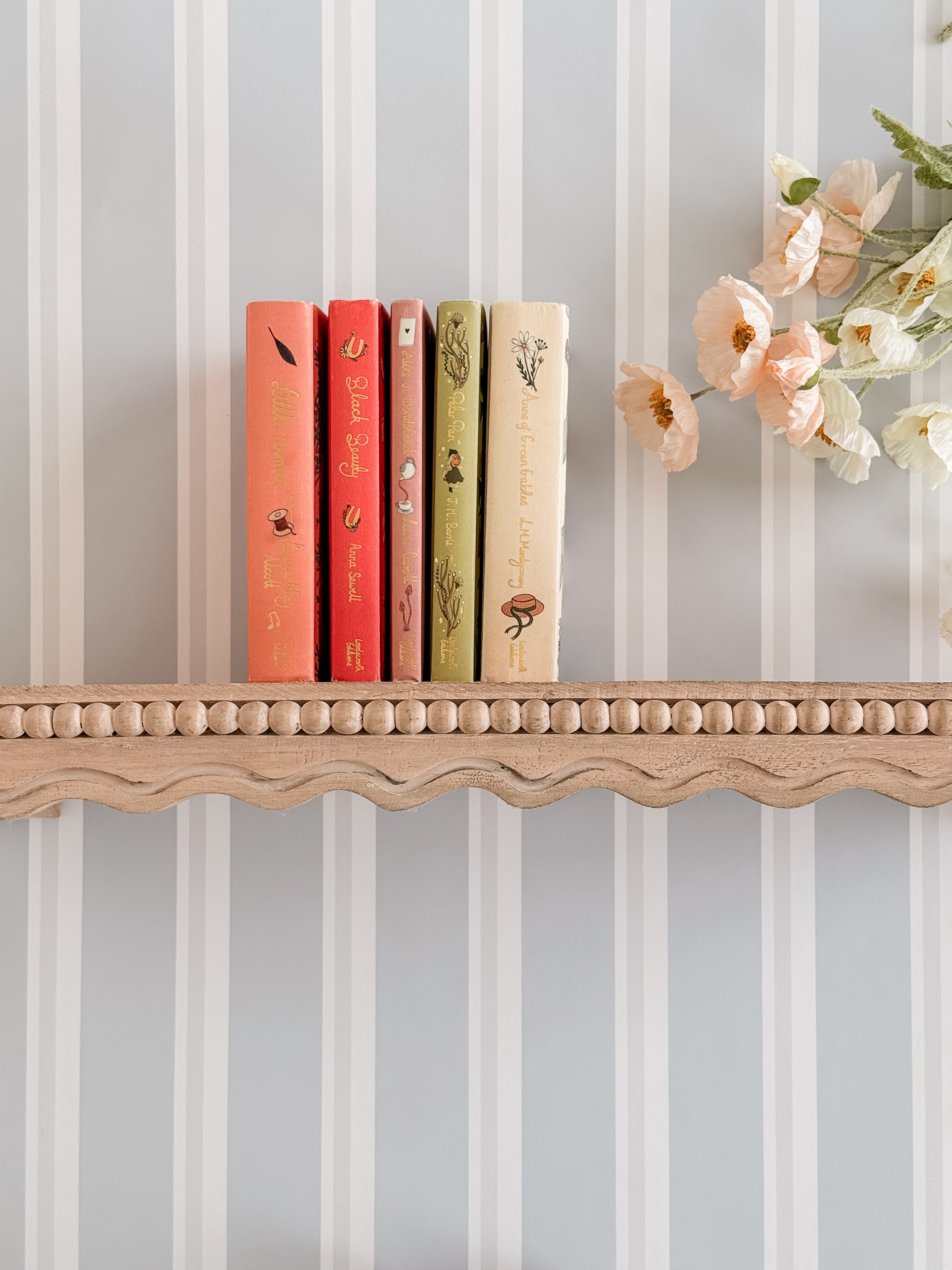 Blue striped wallpaper with beautiful scalloped Pottery Barn shelf. Shelf has muted books and a bouquet of flowers.