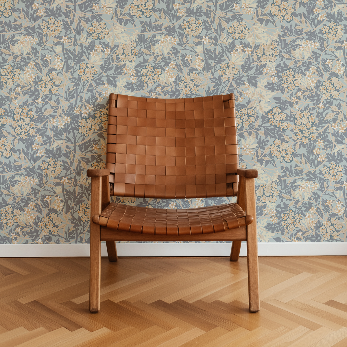 A mid-century modern wooden armchair with a woven tan leather seat and backrest, set against a blue and beige floral wallpaper and a light wood herringbone floor.