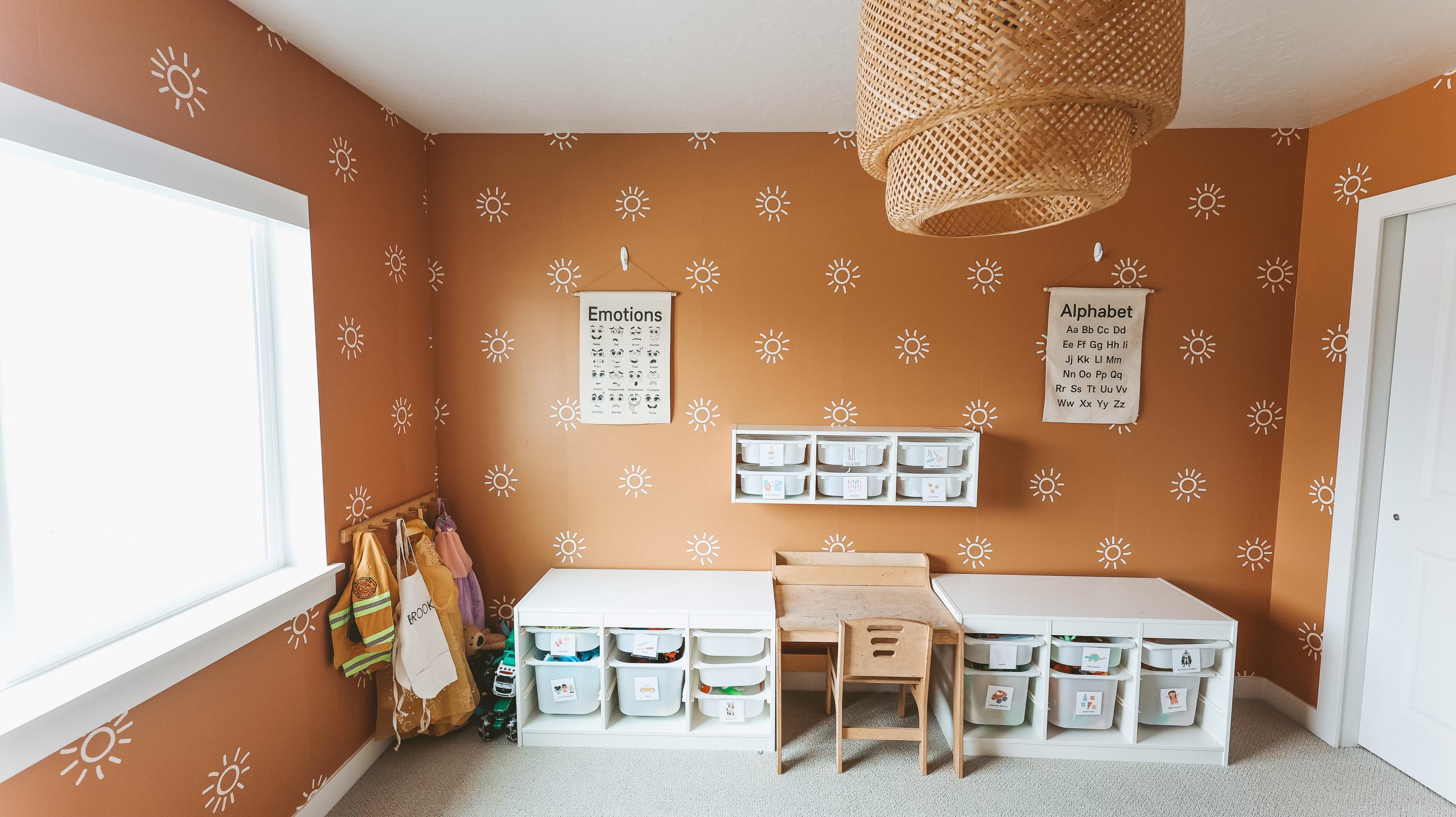 Spacious child's play area with a terracotta wall, white sunburst stickers, and educational charts, illuminated by natural light