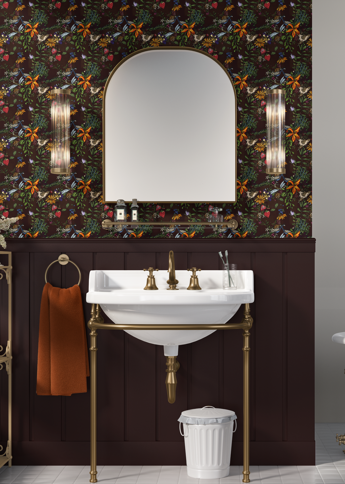Whimsical peacock botanical wallpaper in a moody vintage bathroom with dark plum wainscoting, brass fixtures, arched mirror and white pedestal sink.