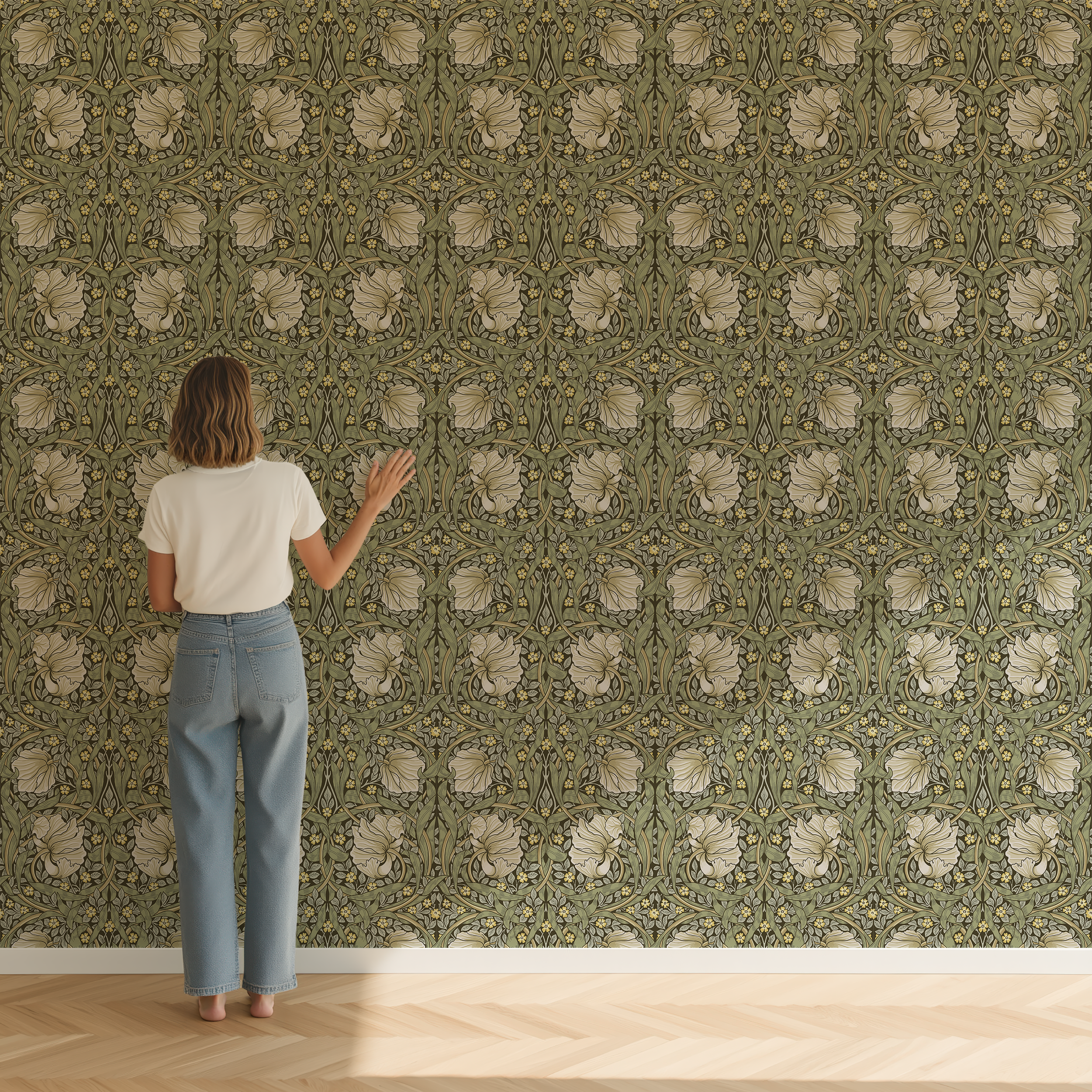 A woman stands with her back to the camera against a wall covered in green and beige floral wallpaper, wearing a white t-shirt and light blue jeans in a room with light wood flooring.