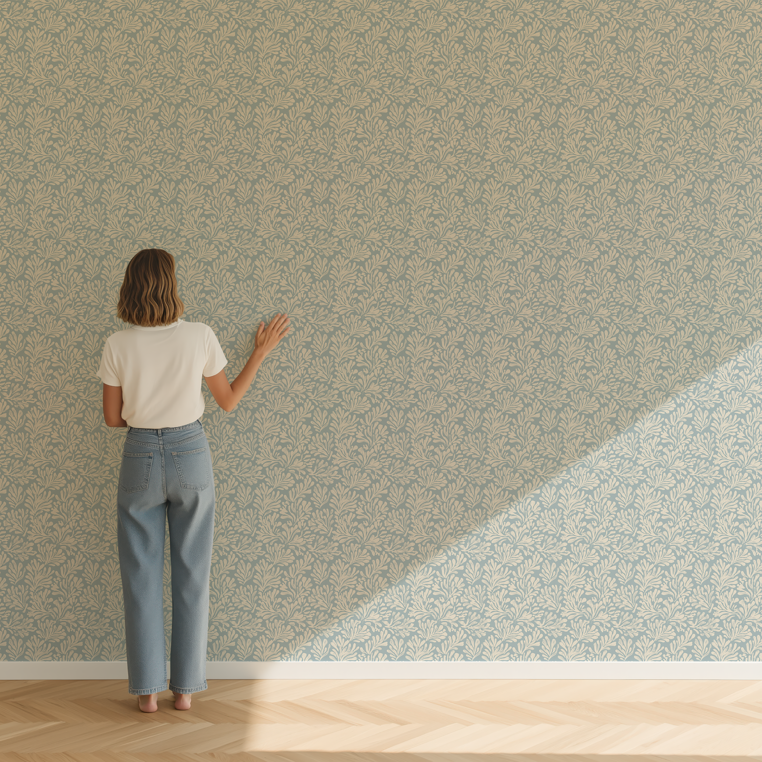 A woman stands with her back to the camera against a wall covered in a delicate blue and beige floral patterned wallpaper, with a diagonal patch of sunlight on the floor.