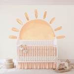 White crib in a nursery with a sunshine wall sticker, rocking horse beside.