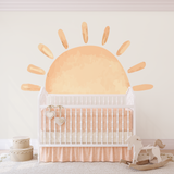 White crib in a nursery with a sunshine wall sticker, rocking horse beside.