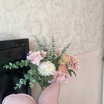 Cozy nursery corner with woodland animal-themed wallpaper in soft beige, adorned with a decorative bouquet and a pink pig-shaped pillow on a small cabinet