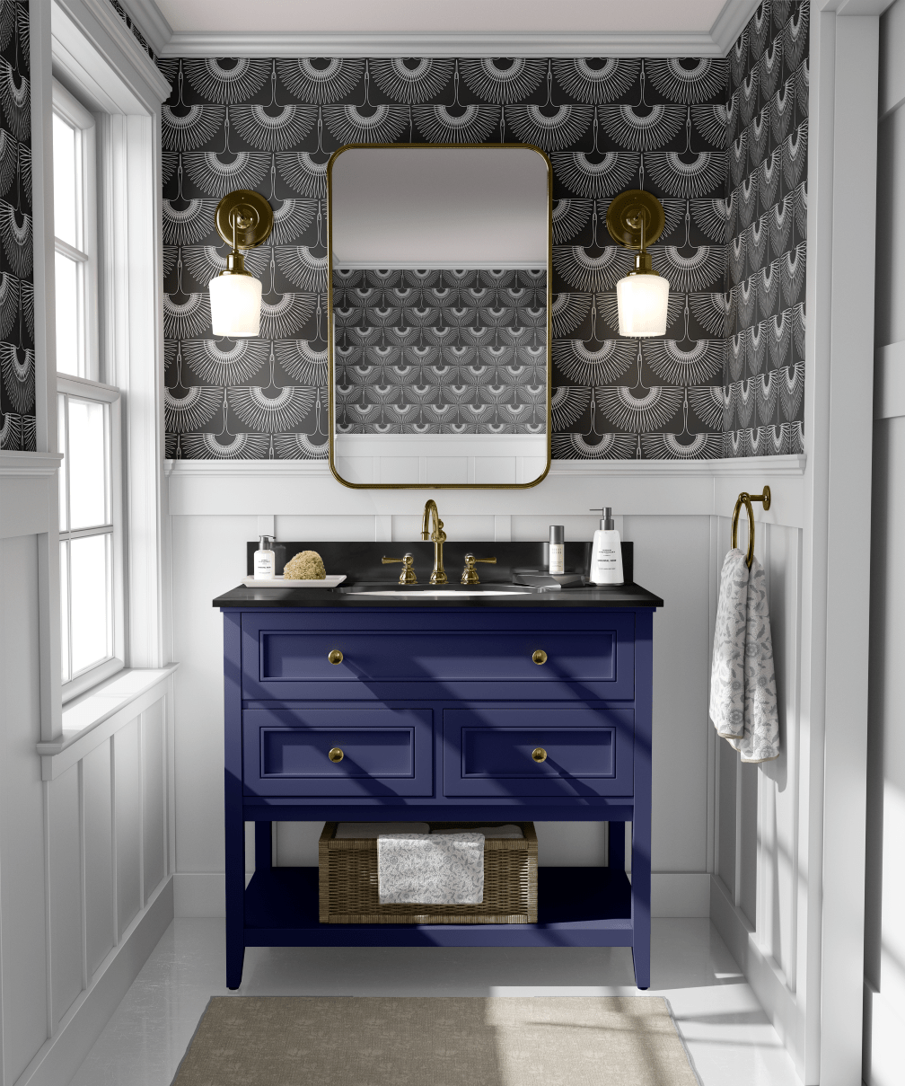 A chic bathroom with black heron-patterned wallpaper, a navy blue vanity, gold fixtures, a rectangular mirror, and brass sconces.