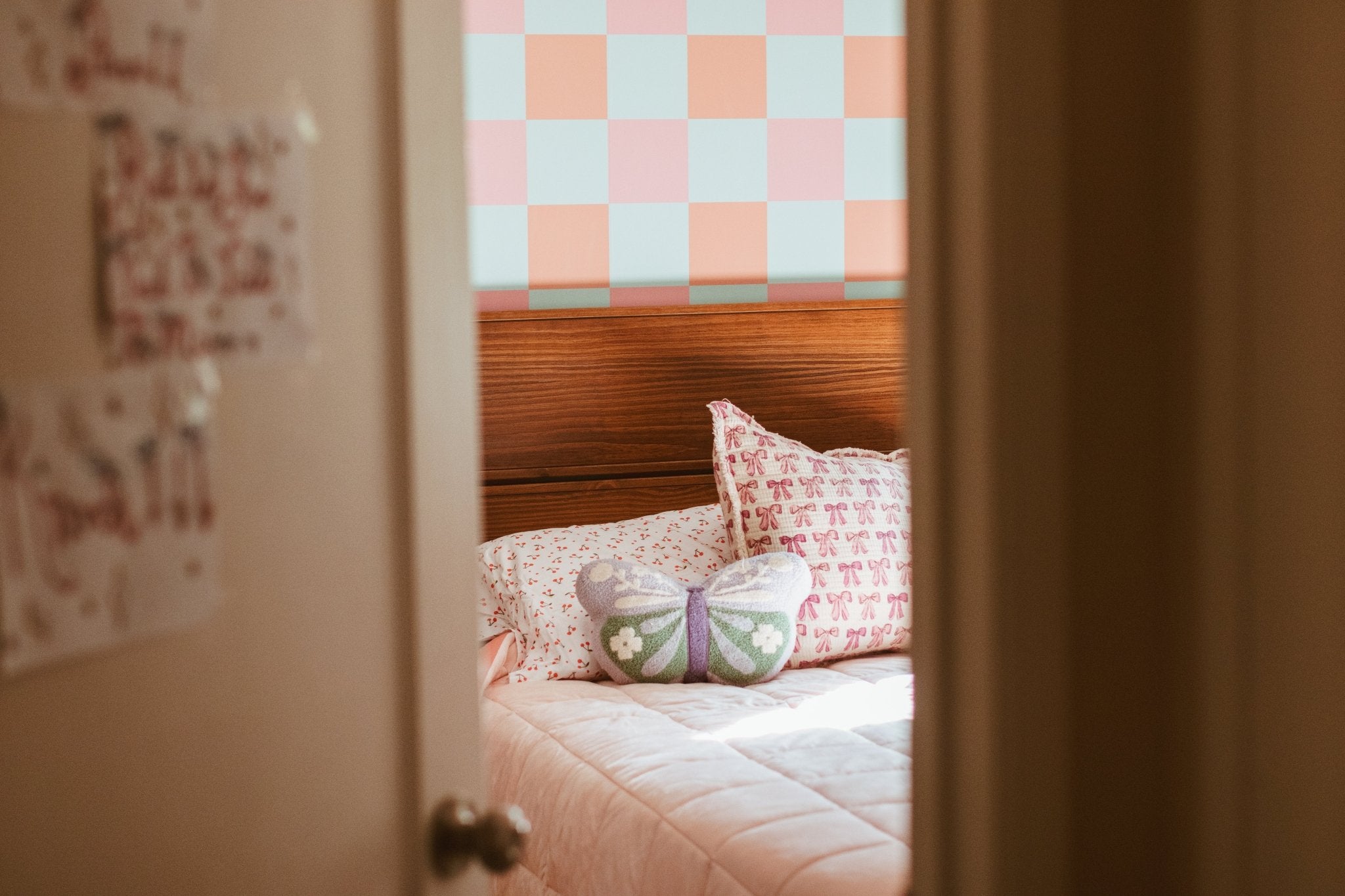 Check wallpaper (orange, pink, and light blue checked) in girl's bedroom with queen bed, pink quilt.