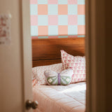 Check wallpaper (orange, pink, and light blue checked) in girl's bedroom with queen bed, pink quilt.