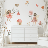 A charming nursery with fairy garden wall decals, showcasing fairies, flowers, and toadstools. The room features a white dresser, a cozy armchair, and soft white curtains, perfect for creating a serene and playful environment for a child.