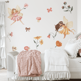 A whimsical girls' bedroom featuring fairy garden decals on the wall, with delicate fairies, flowers, mushrooms, and butterflies. The white bedding with pink accents and floral decor creates a magical and enchanting space