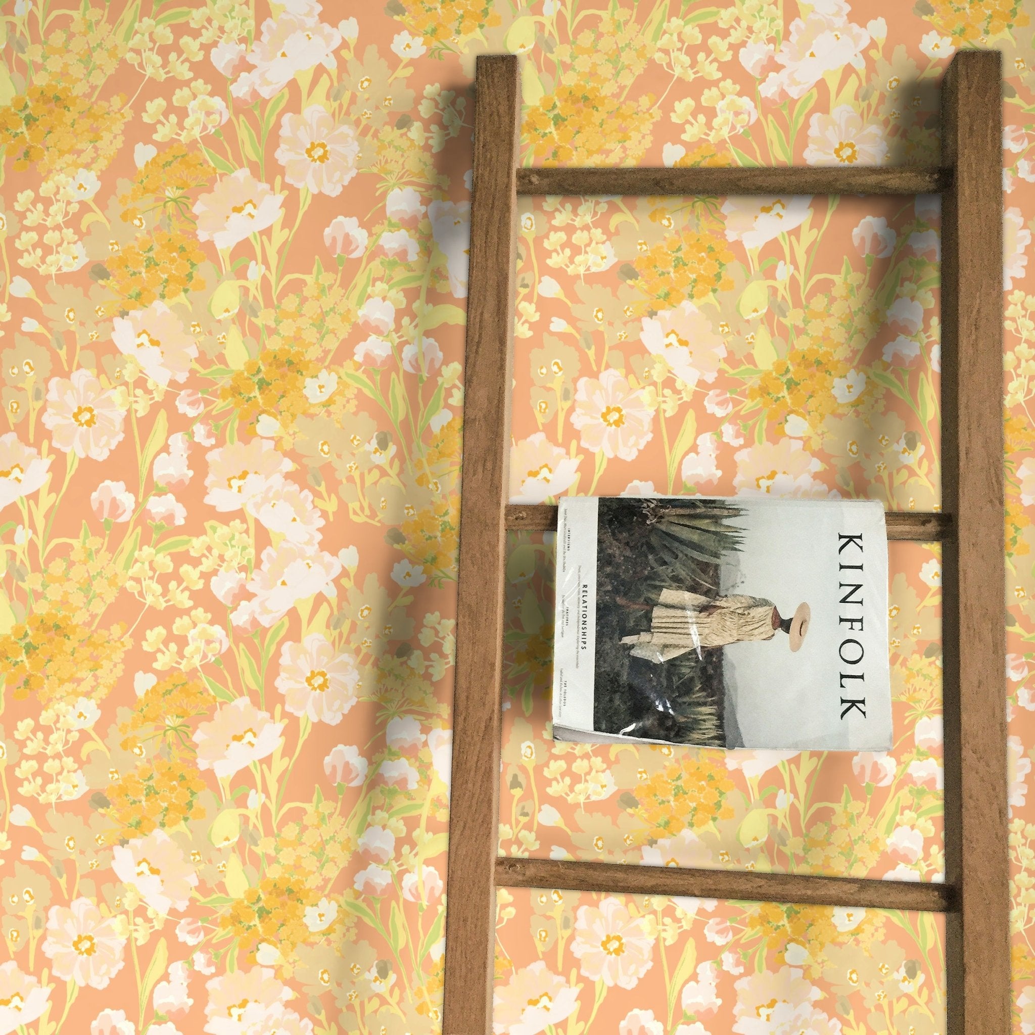 Cheerful floral wallpaper with a pastel peach background, adorned with delicate white, yellow, and pink flowers. A wooden ladder leans against the wall, holding a Kinfolk magazine, creating a charming and inviting atmosphere.