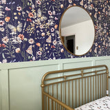 A charming nursery featuring a navy blue wallpaper adorned with detailed floral and butterfly patterns, complemented by a circular mirror and a green half-wall.