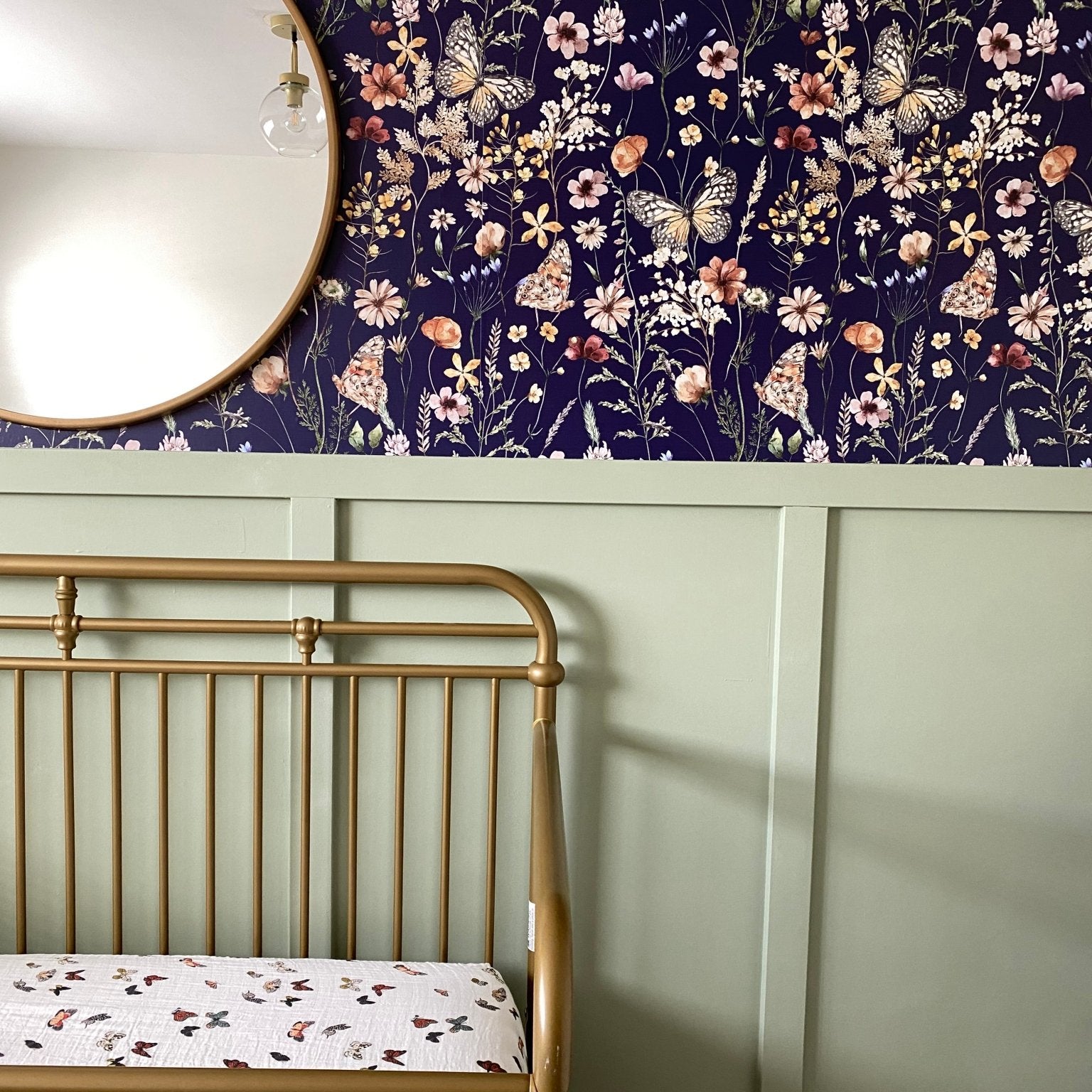 Close-up of the nursery showing the same navy blue butterfly-themed wallpaper and the top of a brass crib against a green half-wall