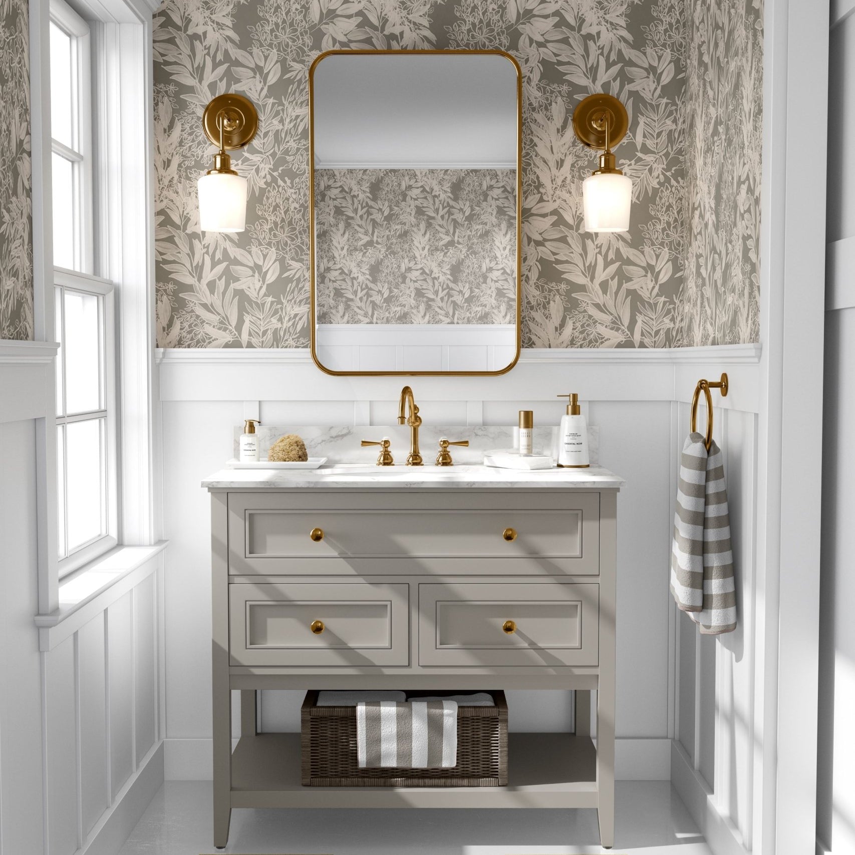 A well-lit bathroom interior with walls covered in a cream leaf pattern wallpaper that matches the previous image, completed with a wooden vanity with gold accents and a rectangular mirror.