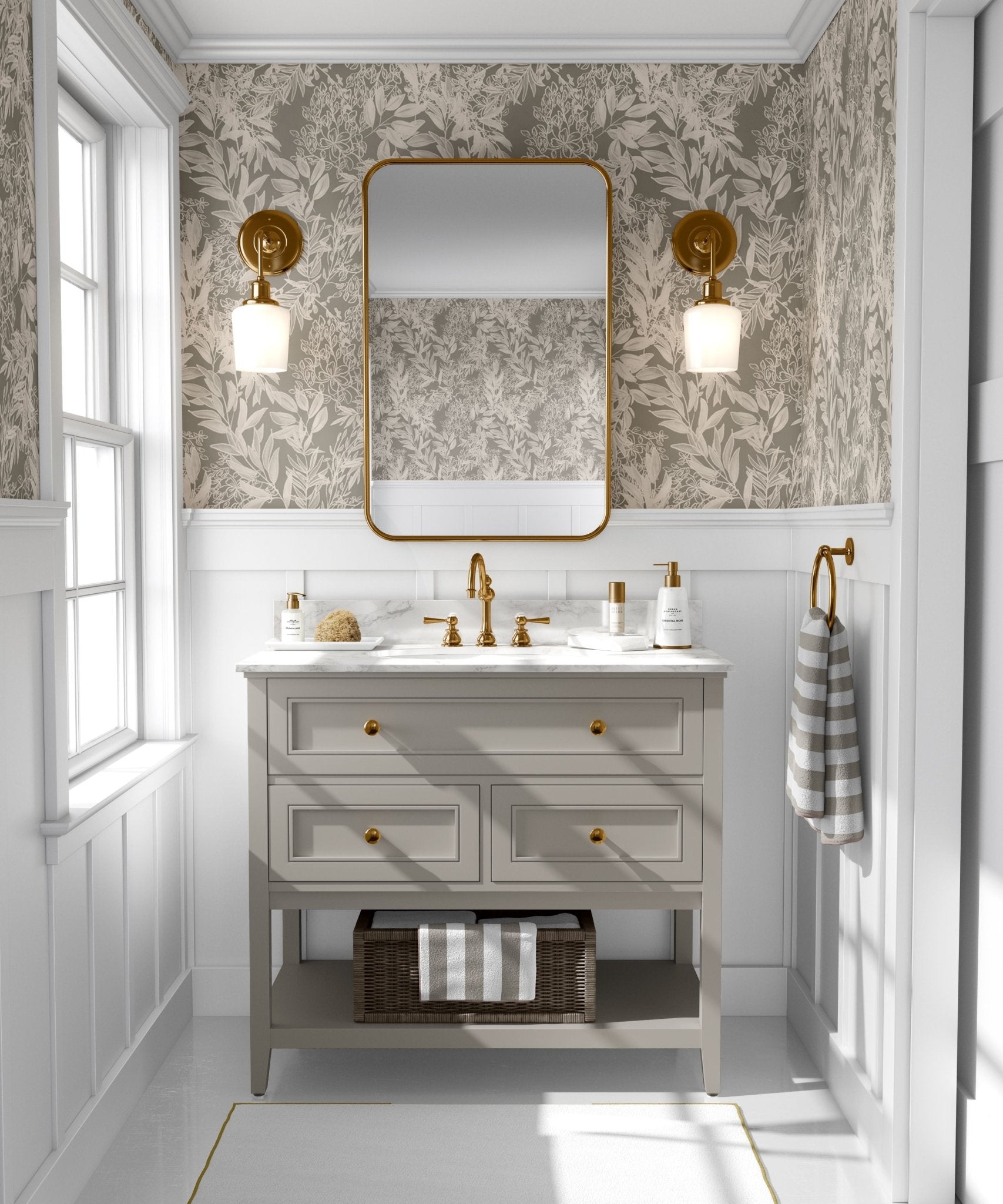 A well-lit bathroom interior with walls covered in a cream leaf pattern wallpaper that matches the previous image, completed with a wooden vanity with gold accents and a rectangular mirror.