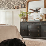 Same bedroom setup showing a sleeping black dog on a plush carpet, enhancing the homey feel. Olive branch wallpaper and black furniture remain consistent.