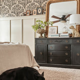  Same bedroom setup showing a sleeping black dog on a plush carpet, enhancing the homey feel. Olive branch wallpaper and black furniture remain consistent.