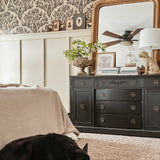 Same bedroom setup showing a sleeping black dog on a plush carpet, enhancing the homey feel. Olive branch wallpaper and black furniture remain consistent.