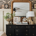 Close-up of the bedroom's decor, highlighting the black dresser adorned with books, plants, and framed pictures against the decorative olive branch wallpaper.