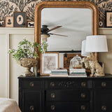 Close-up of the bedroom's decor, highlighting the black dresser adorned with books, plants, and framed pictures against the decorative olive branch wallpaper.