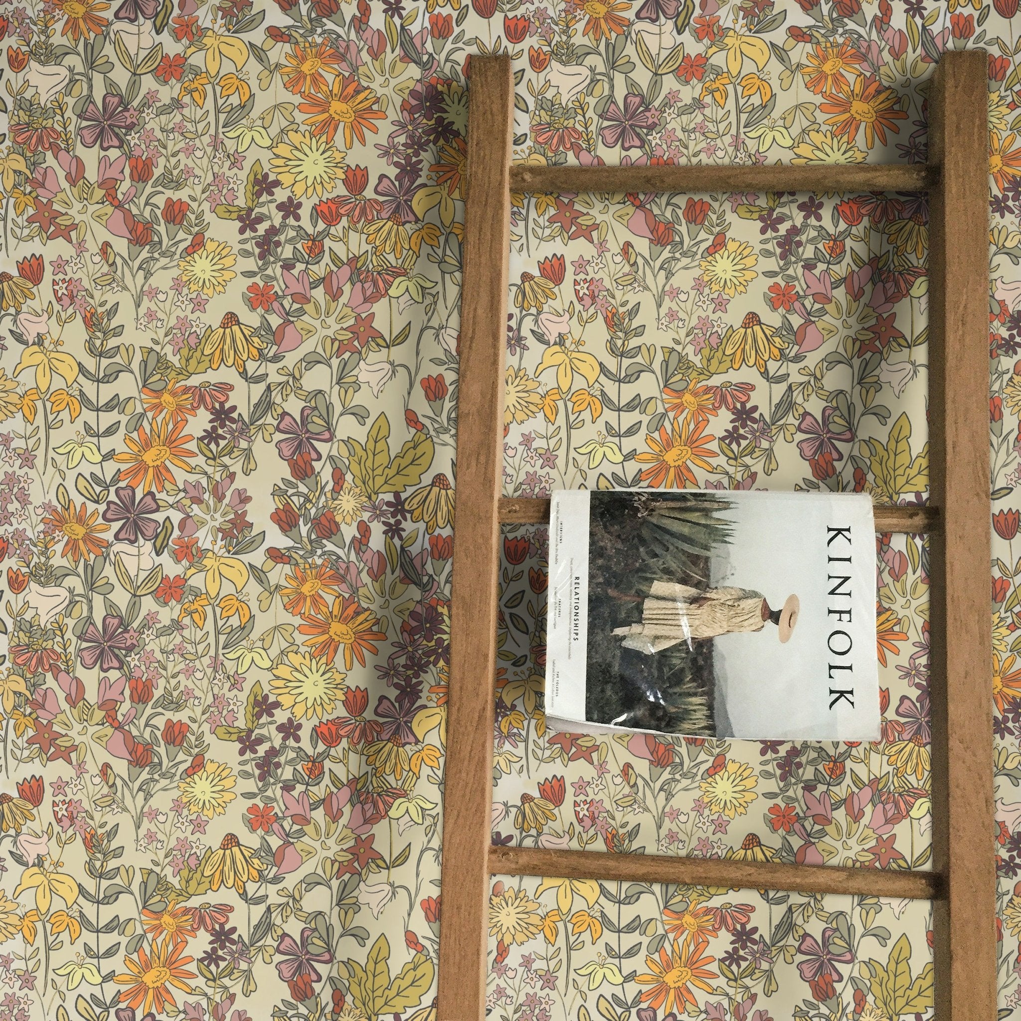 Earthy boho floral wallpaper featuring an array of vibrant flowers in yellow, orange, and purple tones. A wooden ladder leans against the wall with a Kinfolk magazine draped over one rung, adding a rustic touch to the decor.