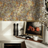 A kitchen staging with summertime floral wallpaper in vibrant colors, highlighting a countertop with a framed painting, black pepper grinders, a vase with flowers, and a window view