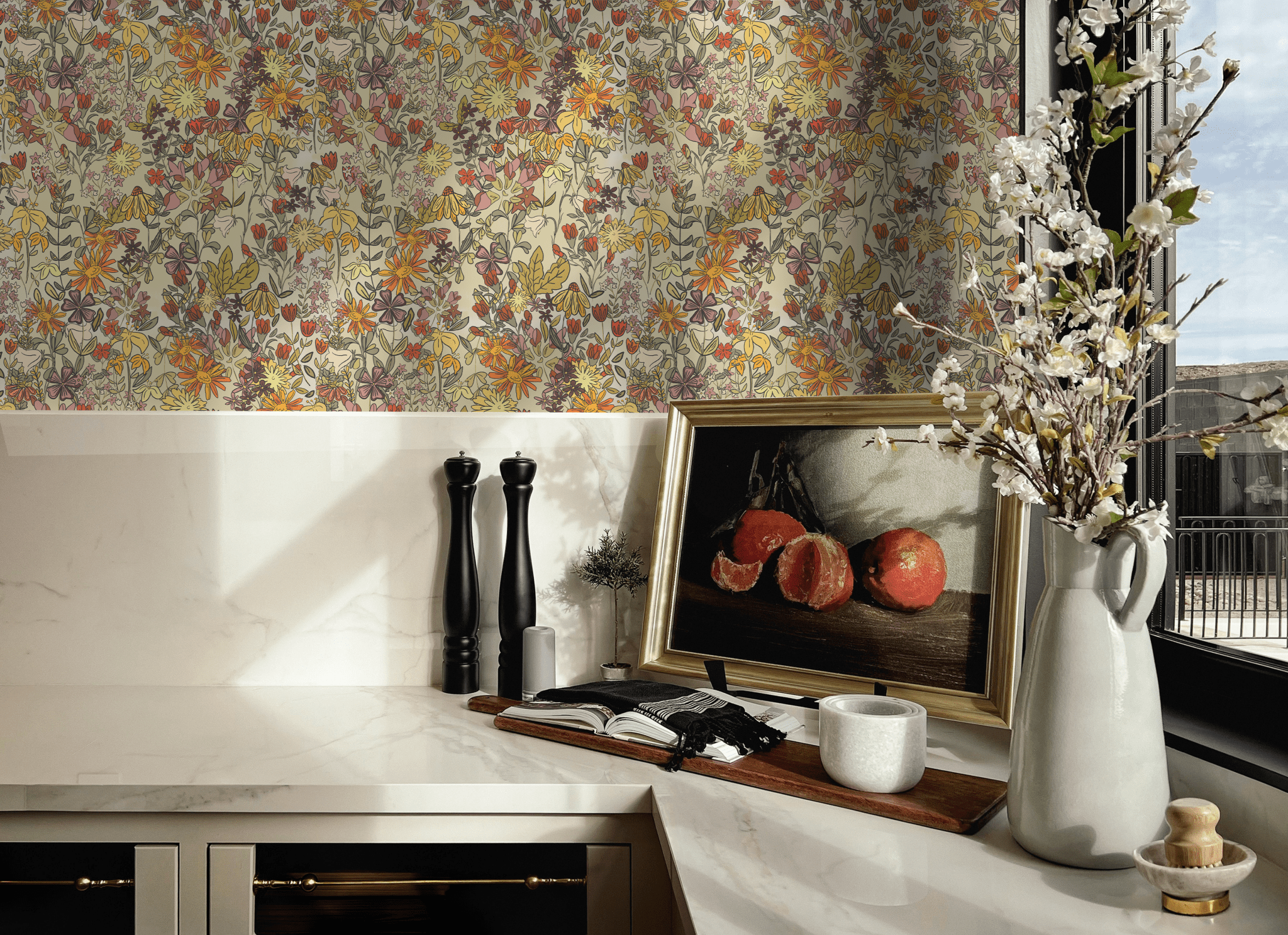 A kitchen staging with summertime floral wallpaper in vibrant colors, highlighting a countertop with a framed painting, black pepper grinders, a vase with flowers, and a window view