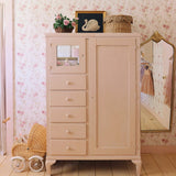 A vintage-inspired room with a pink painted dresser, wicker basket, and floral wallpaper. The dresser is decorated with a framed swan painting and pink flowers, creating a charming, antique aesthetic.