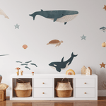 Children's room with whimsical ocean decals; plush dolphin, giraffe toy, and starfish adorn the space alongside wicker baskets.