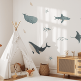 Bright, airy child's room with marine wall decals, a teepee play tent, and a tall plush giraffe next to a modern wooden dresser