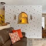A room with a wall covered in beige wallpaper featuring a floral motif with brown and pink flowers. A gold-framed mirror and ornate sconces are on the wall.
