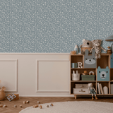 A charming boy's room with blue vine patterned removable wallpaper. A wooden toy shelf is filled with cute animal figures, plush toys, and books. A woven basket and scattered blocks on the floor add a playful touch