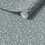 A close-up of a roll of blue vine peel and stick wallpaper with a self-adhesive back. The wallpaper unfurls to reveal a pattern of delicate white florals and vines on a dark blue background.