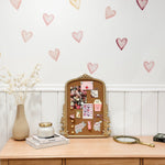 A charming boho-style dresser with a vintage gold-framed corkboard decorated with stickers and notes, flanked by a vase of dried flowers, books, a candle, and a handheld mirror.