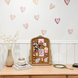A charming boho-style dresser with a vintage gold-framed corkboard decorated with stickers and notes, flanked by a vase of dried flowers, books, a candle, and a handheld mirror.