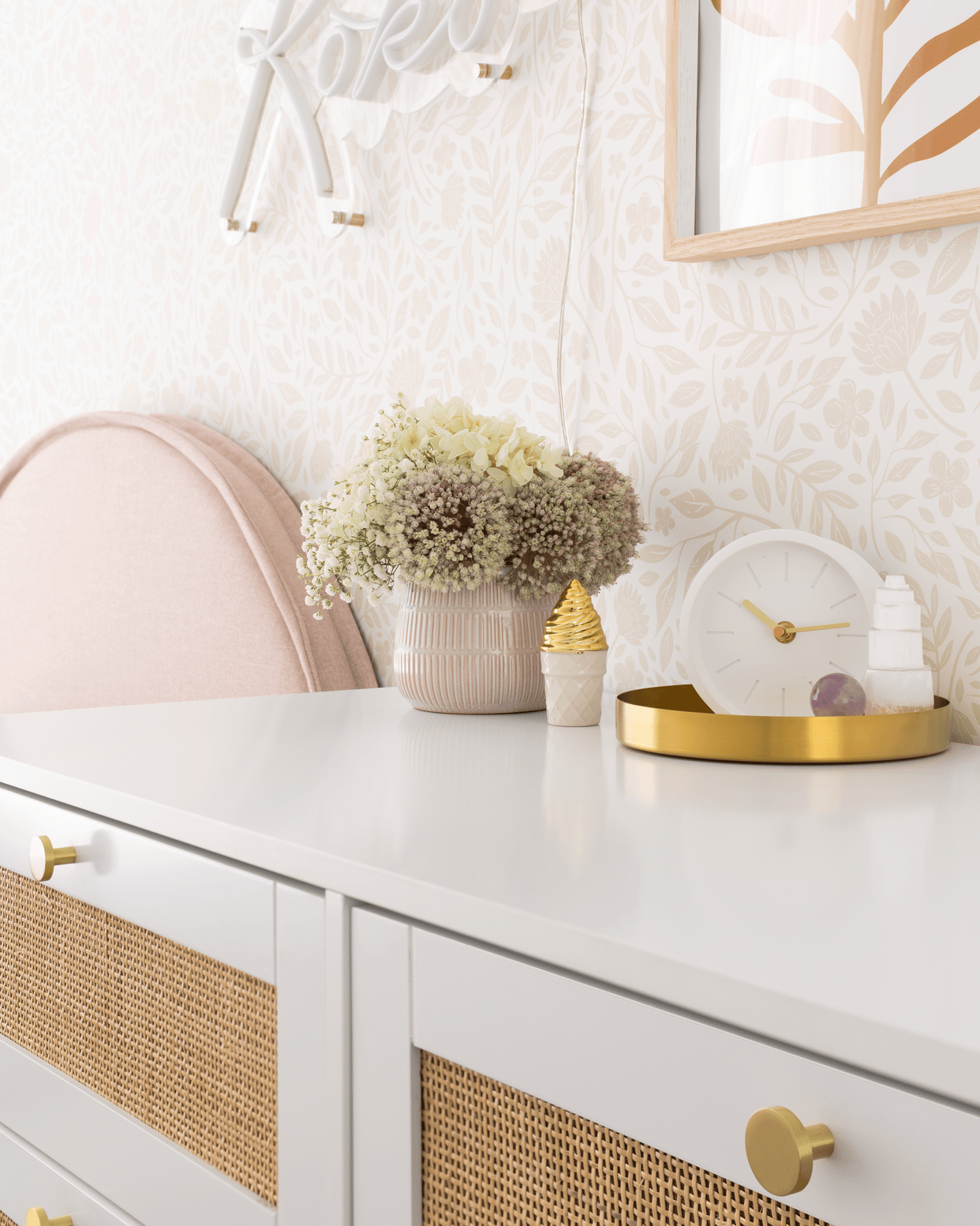 Flower wallpaper behind a white dresser with gold accents