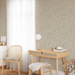 A room corner with beige floral wallpaper, rattan chair, wooden desk, and sheer-curtained window.