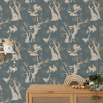 A whimsical children's room featuring a wallpaper with a repetitive pattern of white rabbits in various poses amongst trees and foliage on a blue background. 