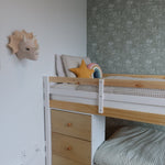 A cozy corner of a child's bedroom with a pine bunk bed, forest green floral wallpaper, and assorted plush toys and cushions.