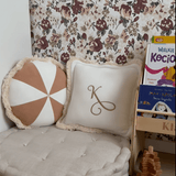 A cozy reading nook with a large cushioned floor seat, decorative pillows, and a floral wallpaper featuring maroon and taupe flowers