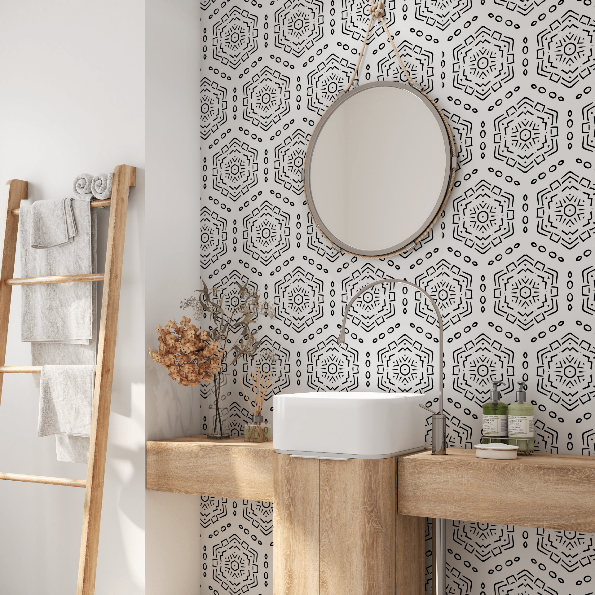 A well-lit bathroom with a white basin sink mounted on a wooden countertop, a circular mirror above it, and a black and white hexagon patterned peel and stick wallpaper. A wooden ladder shelf holds folded gray towels to the left.