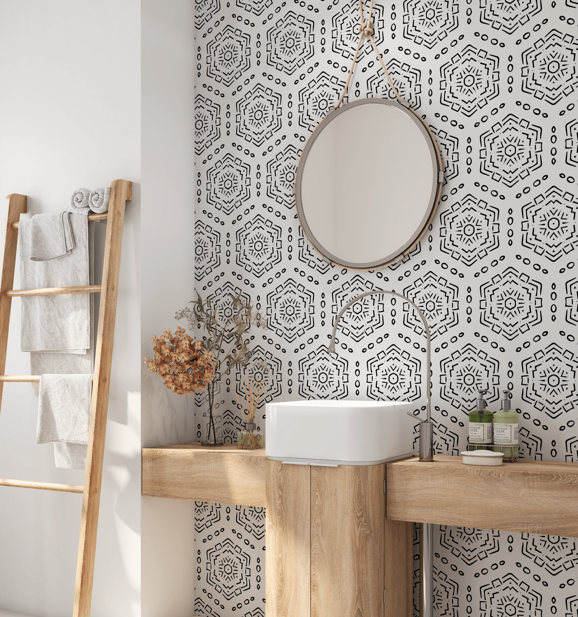 A well-lit bathroom with a white basin sink mounted on a wooden countertop, a circular mirror above it, and a black and white hexagon patterned peel and stick wallpaper. A wooden ladder shelf holds folded gray towels to the left.