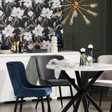 A modern dining area with the same magnolia wallpaper, which acts as a bold backdrop to a white table, blue velvet chairs, and a striking gold light fixture.