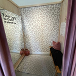 Clothing store change room with a neutral animal print wallpaper feature wall, large mirror and dusty rose curtains.