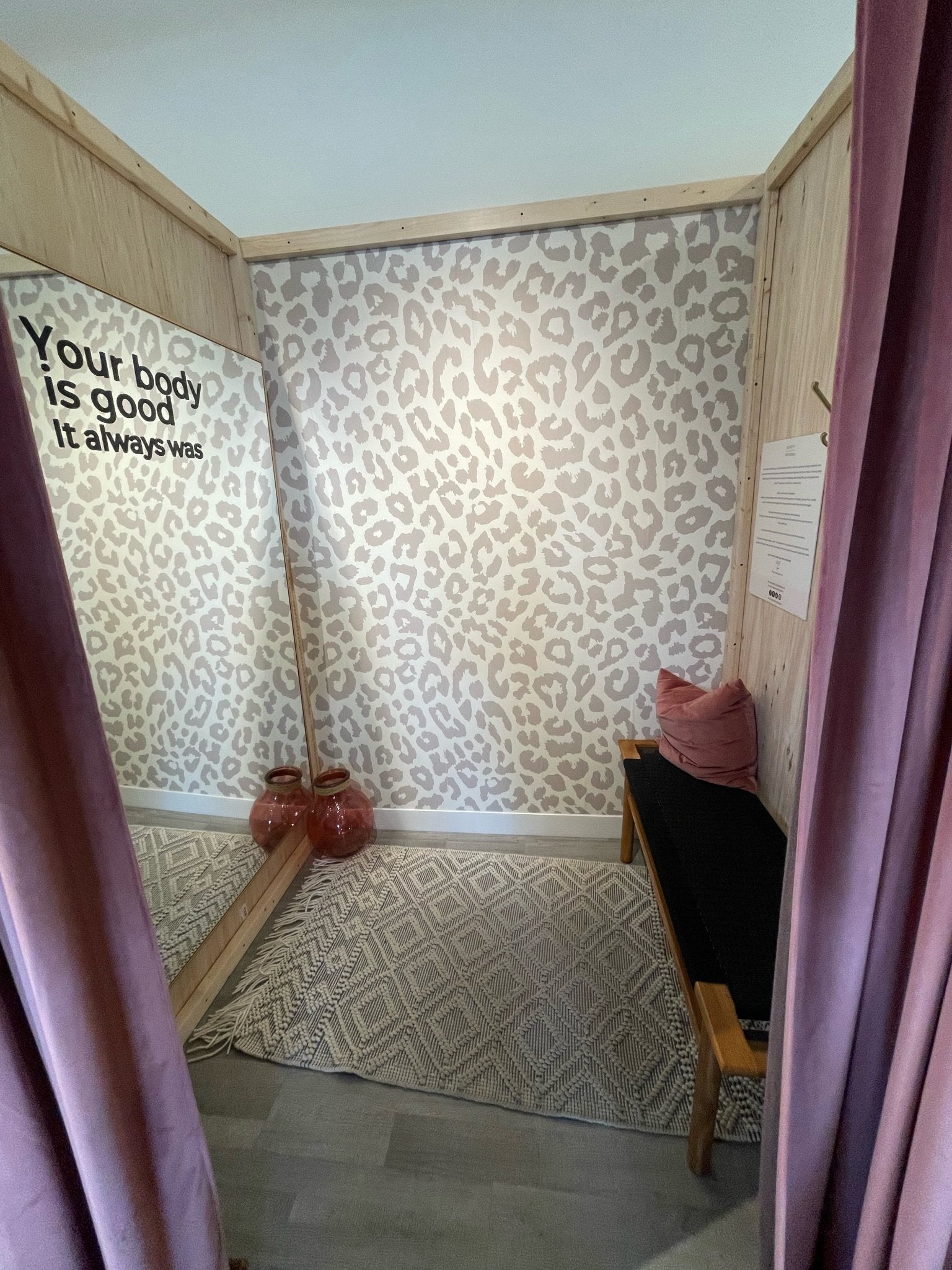 Clothing store change room with a neutral animal print wallpaper feature wall, large mirror and dusty rose curtains.
