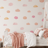 Interior of a girl's bedroom featuring walls with pink and orange watercolor cloud stickers, a cozy bed with pink bedding, and a white canopy with fairy lights