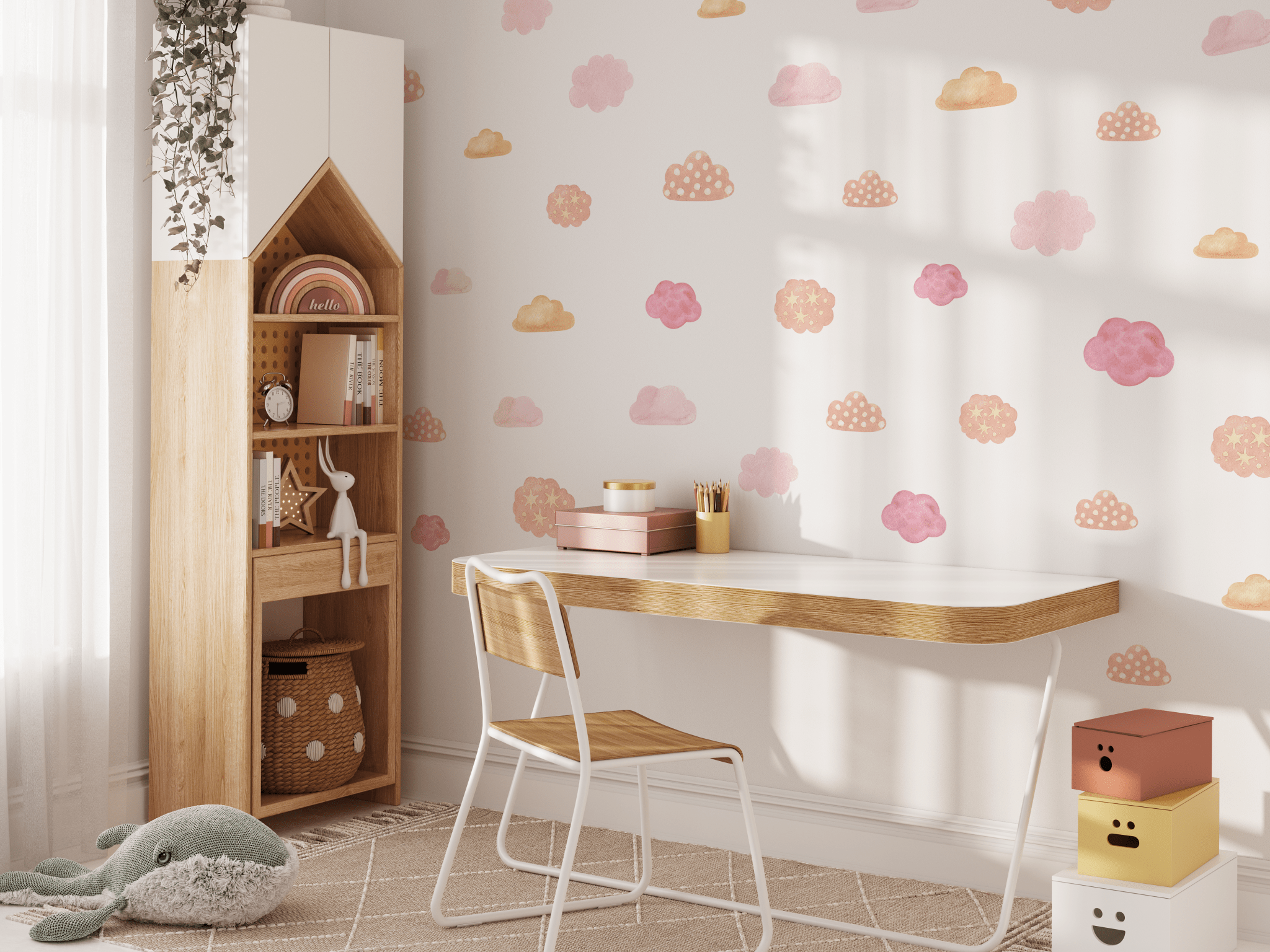 A nursery room wall decorated with watercolor wall stickers of clouds in shades of pink and gold, with a wooden toy rainbow on a cabinet and a hanging plant."