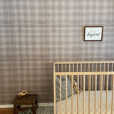 A cozy nursery with a wooden crib and plush toy, wooden stool with a car toy, knitted booties, and a "long live boyhood" wall frame.